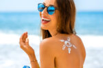 Young woman with sun shape on the shoulder holding sun cream bottle on the beach.