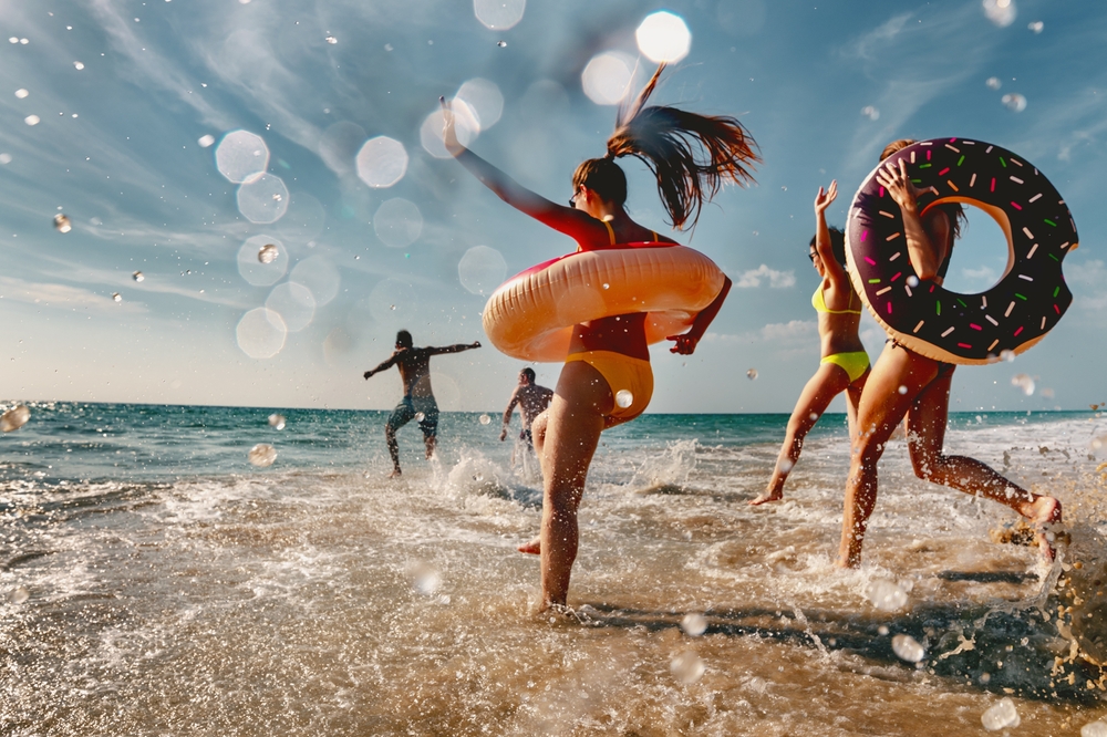 group of friends are having fun and running to sea beach with inflatable donuts